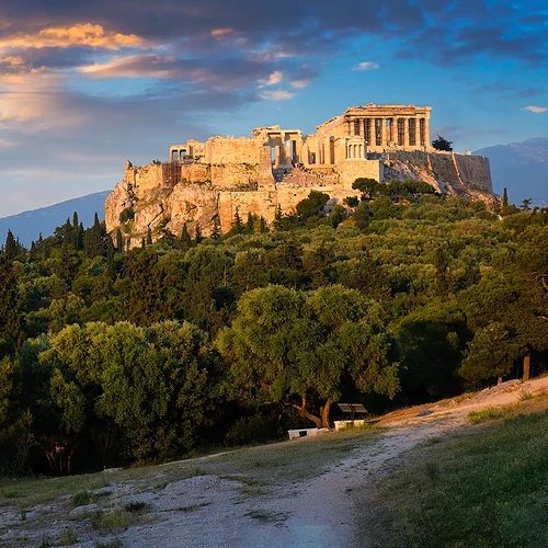 Akropolis i Aten, Grekland, med Parthenon-templet på toppen av berget, omgiven av grönskande träd och en vacker solnedgång i bakgrunden.