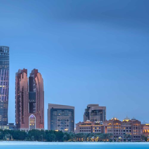 Moderna skyskrapor och historiska byggnader i Dubai skyline vid solnedgången, med tydliga ljusreflektioner och en klar blå himmel, visar stadens unika blandning av tradition och innovation.