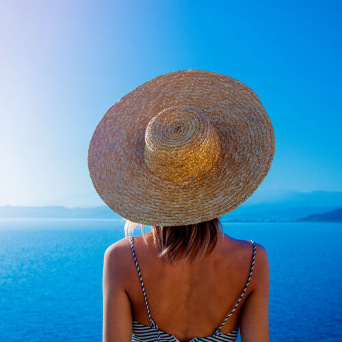 en tjej med stråhatt på Mykonos i Grekland som tittar utöver ett blått hav 