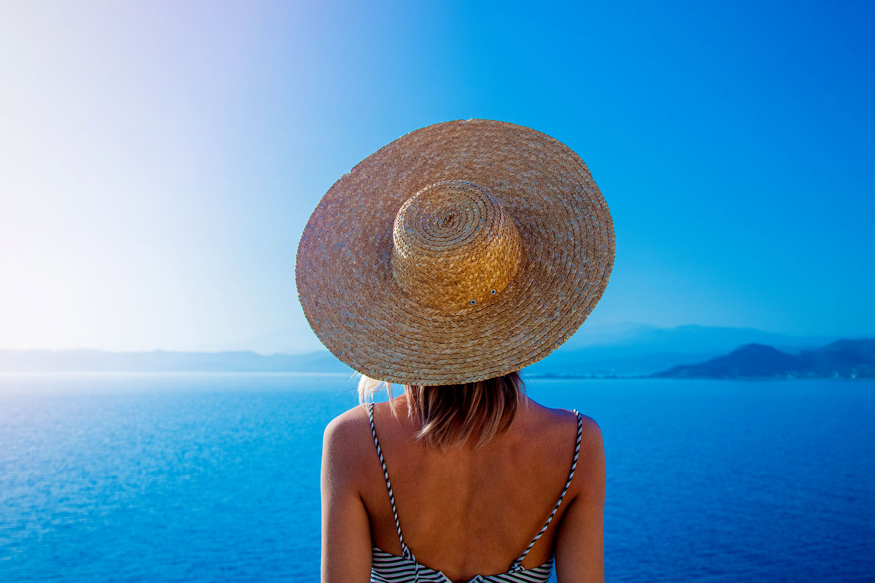 en tjej med stråhatt på Mykonos i Grekland som tittar utöver ett blått hav 