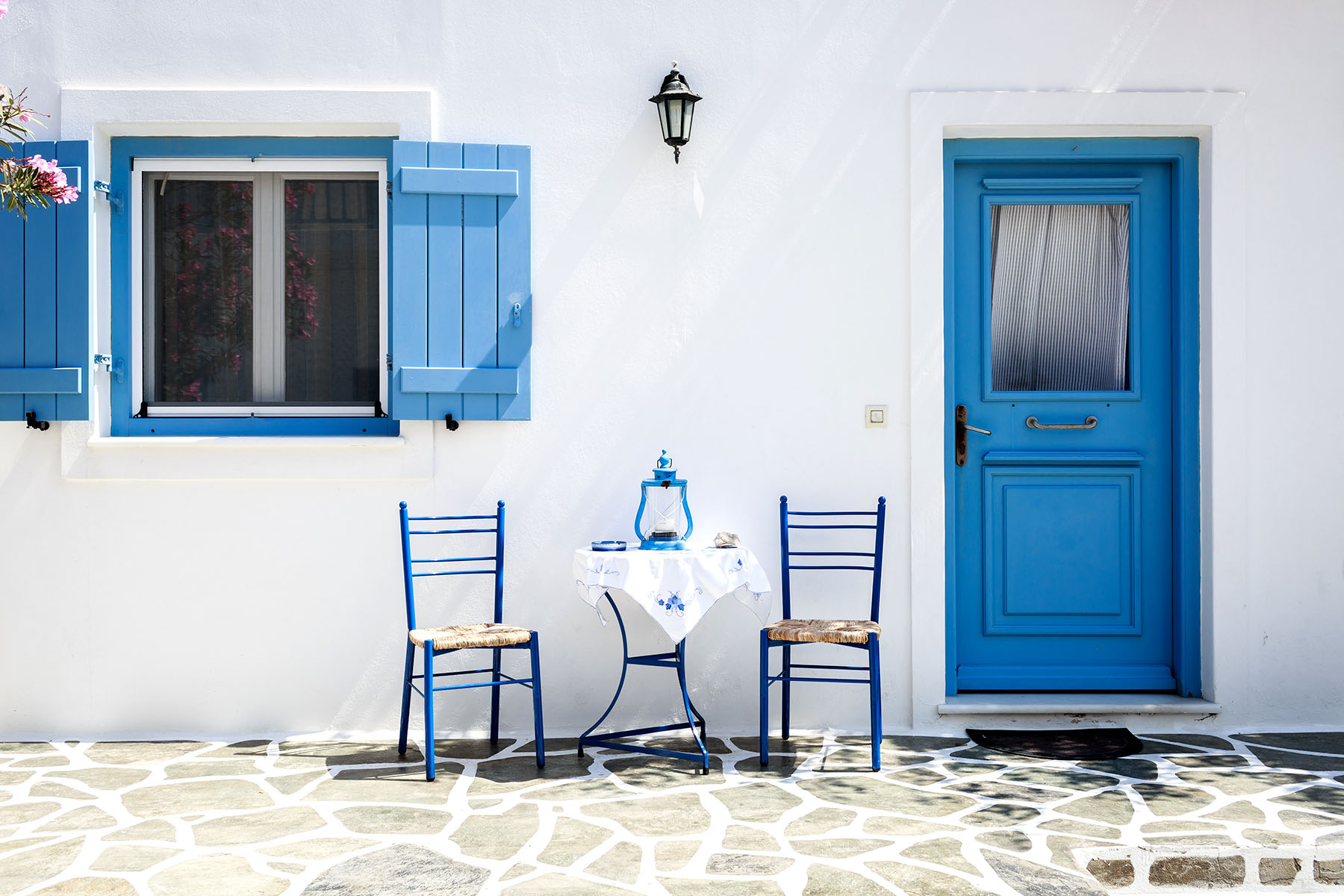 Två stolar och ett bord utanför ett grekiskt hus med vita kalkväggar och blåmålade dörrar