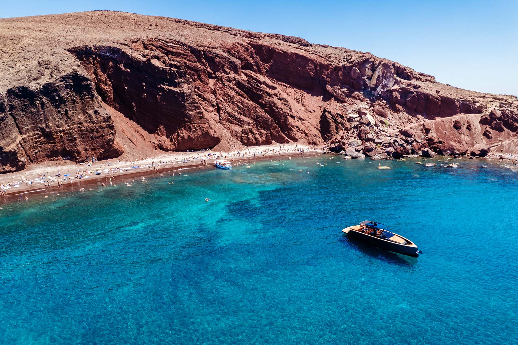 En båt ligger precis utanför en strand på Santorini