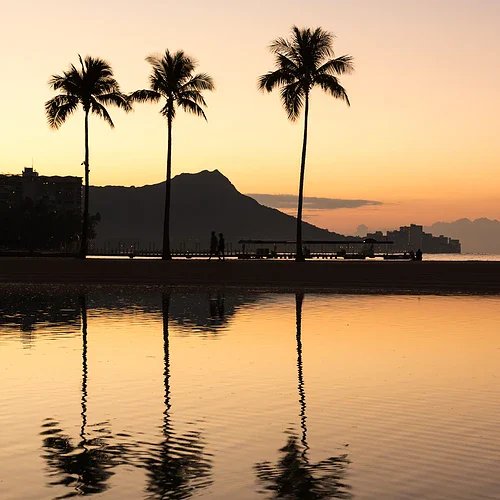 Waikiki på Hawaii i solnedgång med personer som går vid kanten av poolen och stranden
