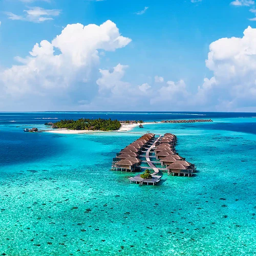 Bild av en tropisk ö i Indiska oceanen med klart turkost vatten, vita sandstränder och en flytande brygga med bungalows. Perfekt för avkoppling och solsemester.