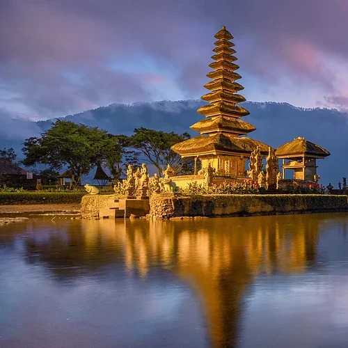 En vacker bild av en traditionell pagod vid en lugn sjö i Indonesien, med en dramatisk solnedgång i bakgrunden och omgivande gröna landskap.