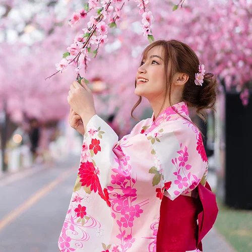 En ung kvinna i traditionell kimono njuter av blommande körsbärsträd i Japan under våren, omgiven av rosa blommor och en lugn atmosfär.