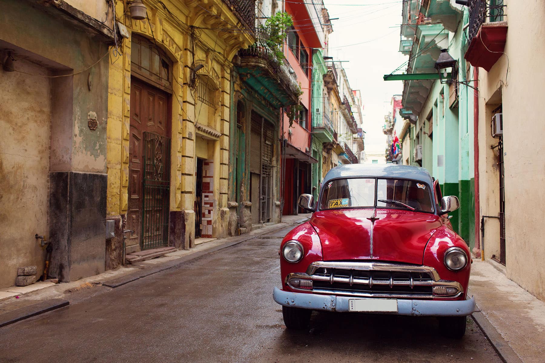 en gatubild i Havana på Kuba med en typisk Kubansk bil i rött