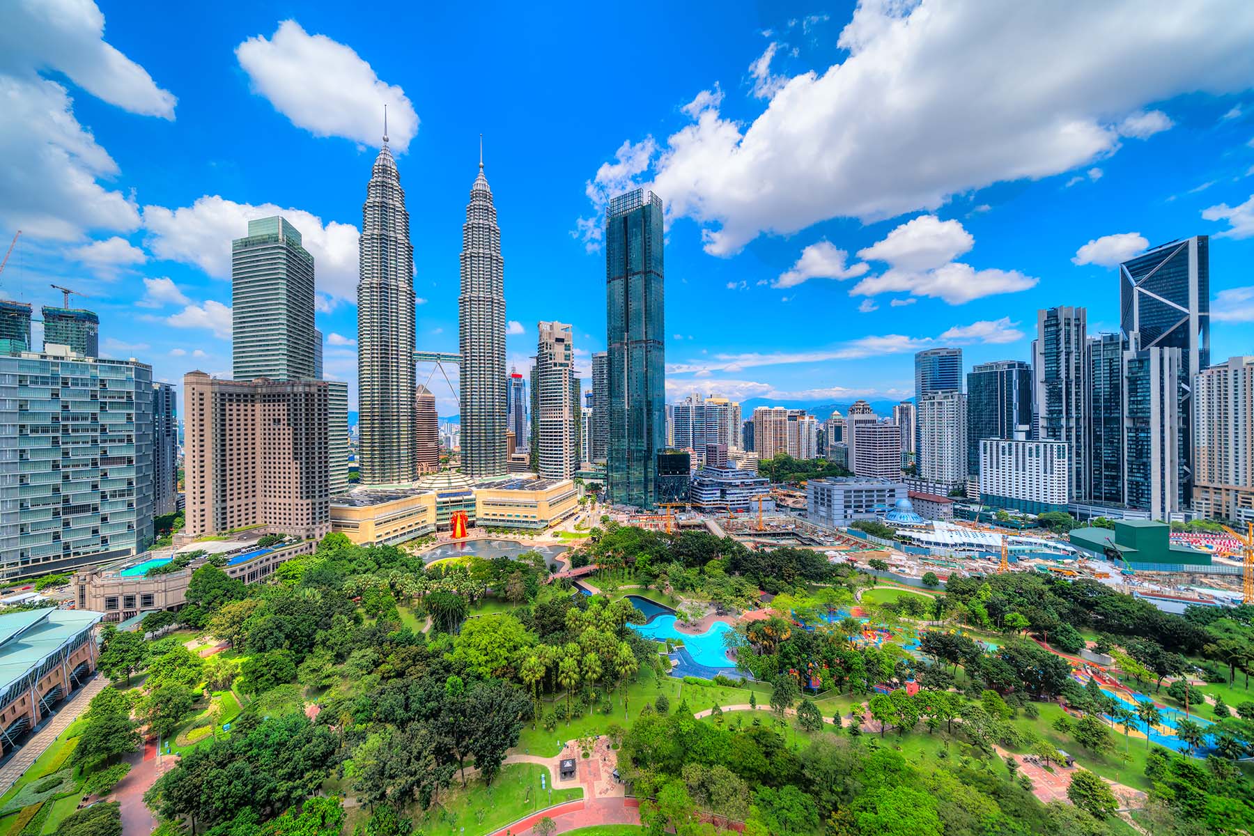Fyrsternaturtorn och modern stadssilhuett i Kuala Lumpur, Malaysia, med gröna parker och höga skyskrapor under en klar blå himmel.