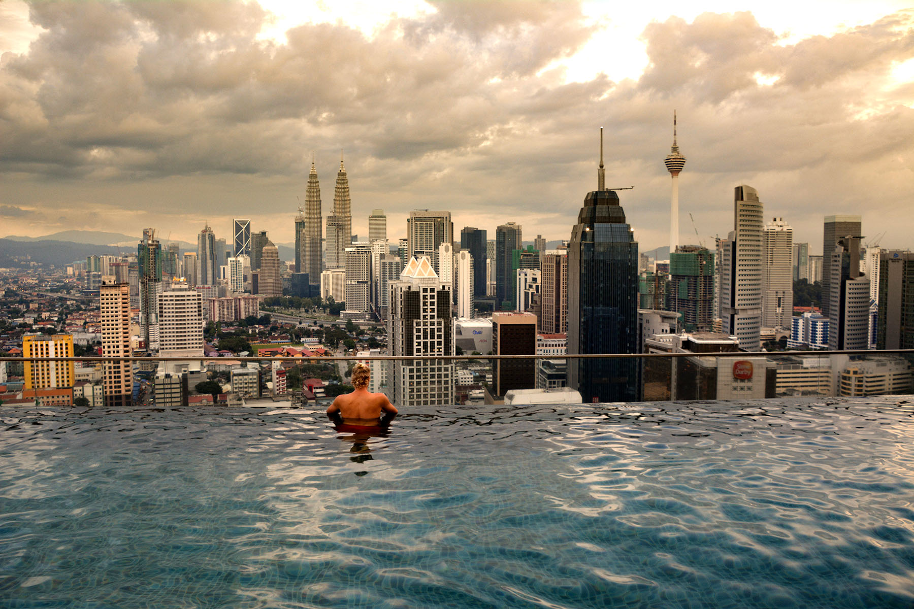 Himmel och skyline med skyskrapor i Kuala Lumpurs stadssilhuett, syns från infinitypool på taket under solnedgången, lyx och utsikt.