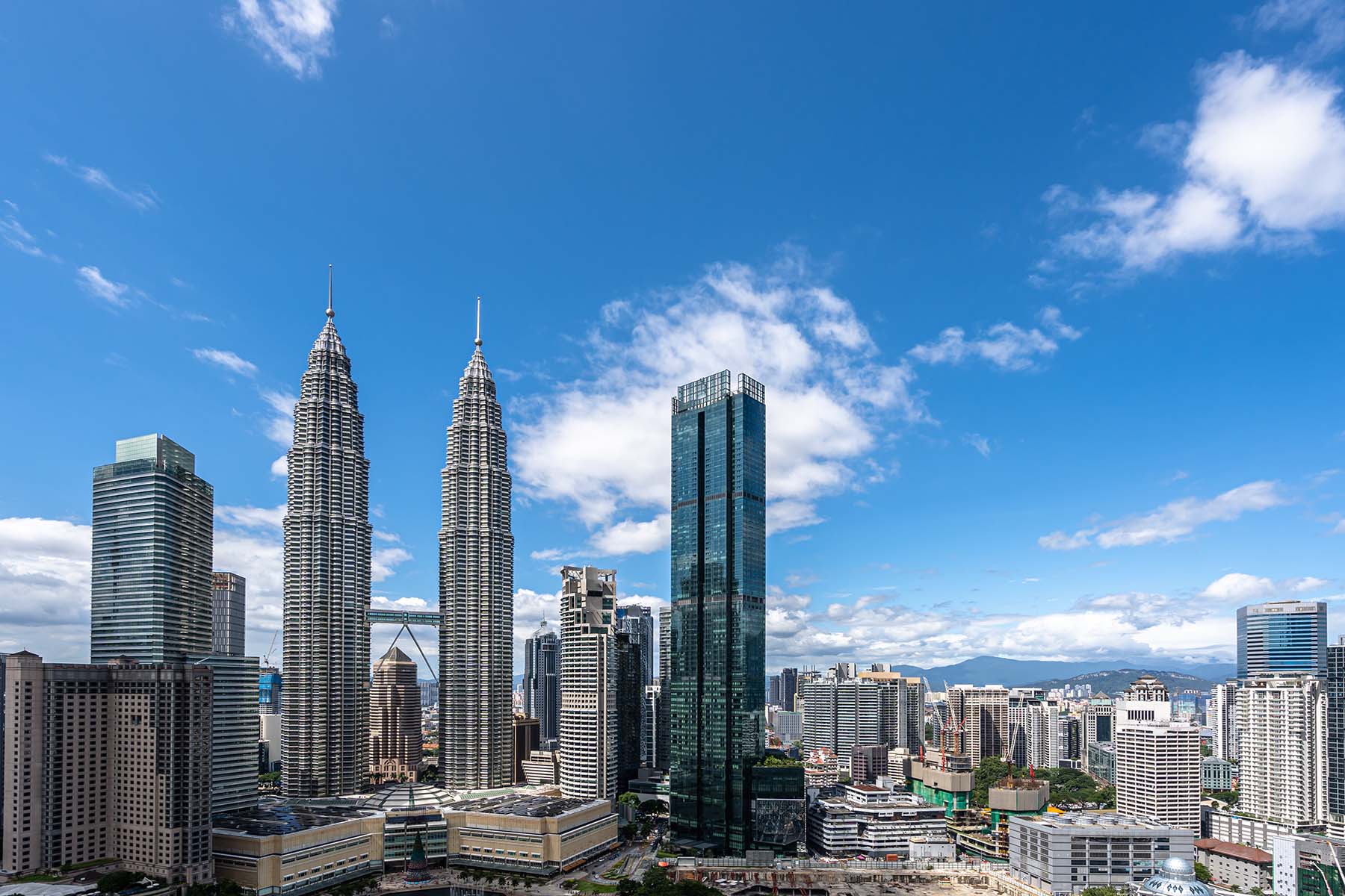 Futuristisk stadsbild med Petronas-tornen och modern skyskrapa i Kuala Lumpur mot en klar blå himmel.