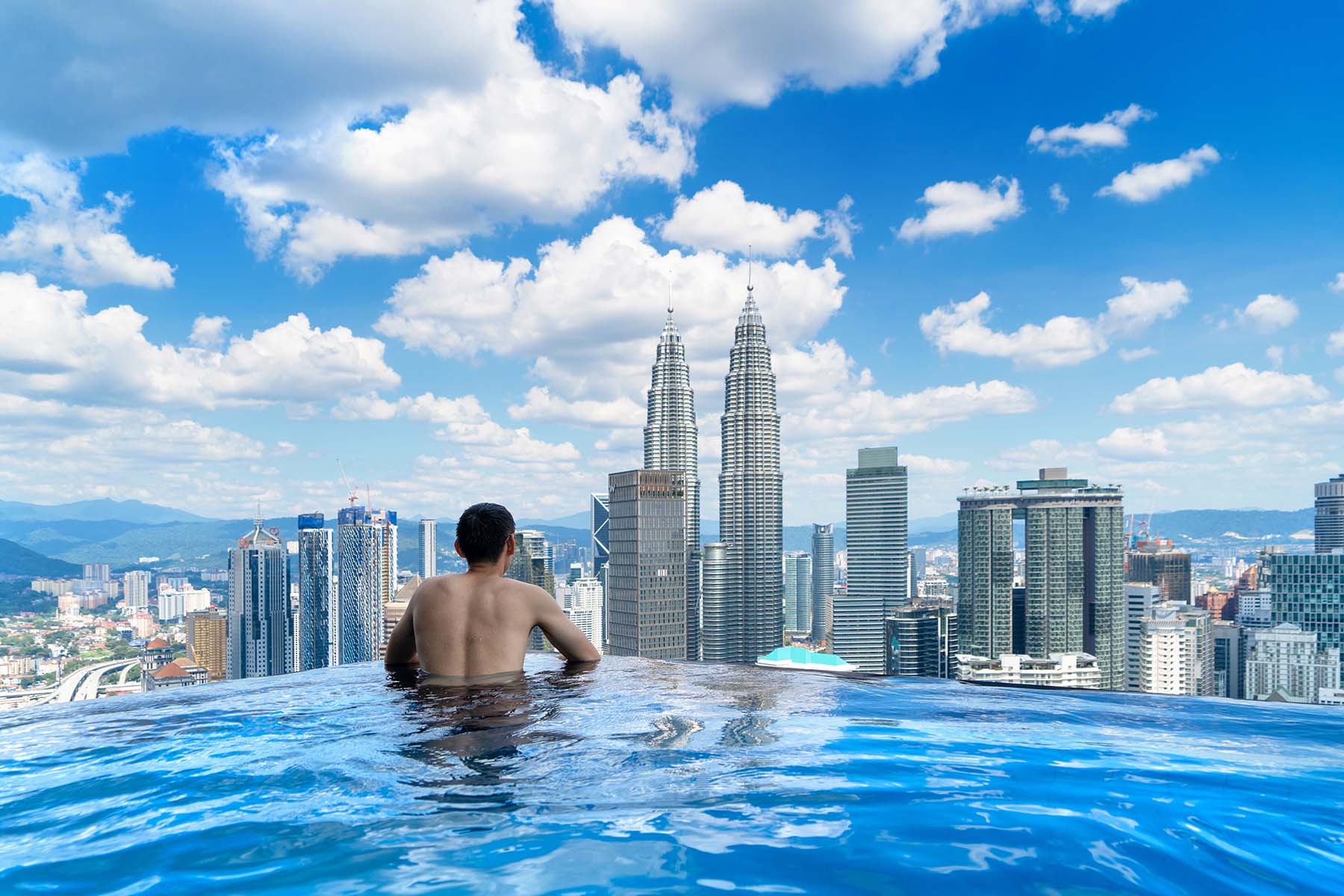 1. En man som badar i en infinity-pool med utsikt över Kuala Lumpur och Petronas Twin Towers en klar solig dag i Malaysia.