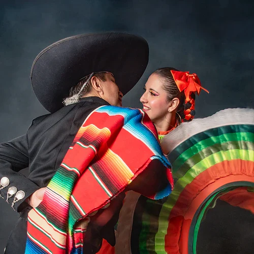 Ett mexikansk par traditionella mexikanska kläder dansar och ler mot varandra.