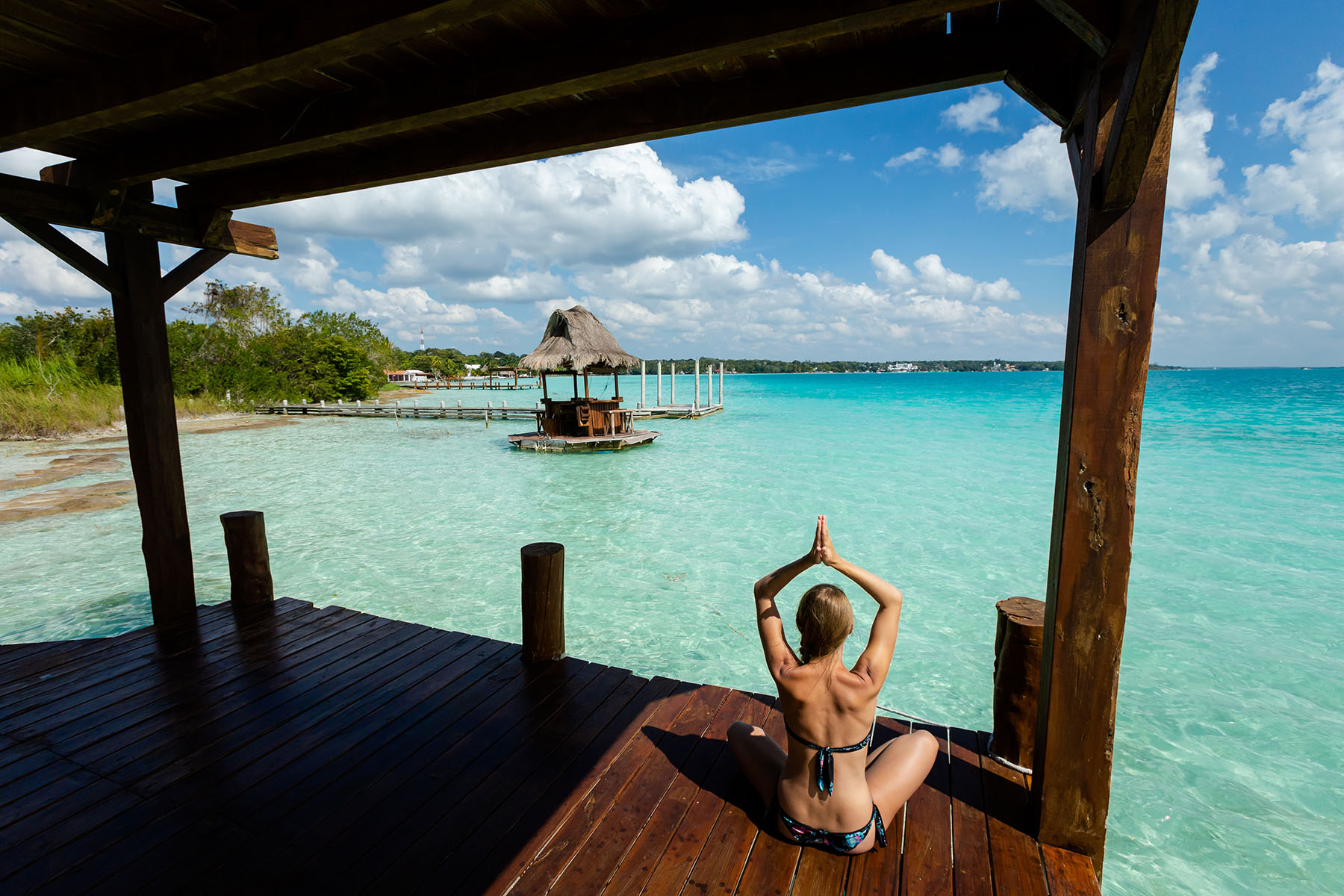 En kvinna sitter på en balkong och utför yoga med utsikt mot stranden i Riviera Maya