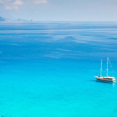 Fritidsbåt seglar på klart blått hav nära grönskande kustlinje under en solig dag.