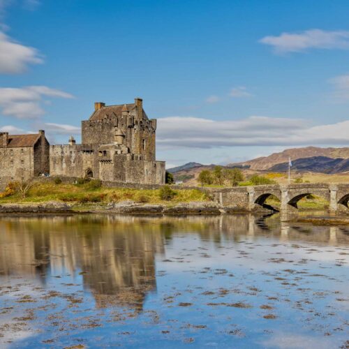 En bild av ett historiskt skotskt slott beläget vid en spegelblank sjö, omgiven av natursköna landskap och berg i bakgrunden. Perfekt för att visa Skottlands rika kulturarv och natursköna skönhet.