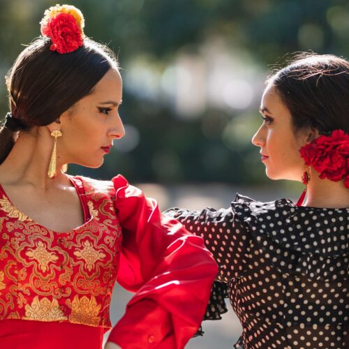 En bild av två flamencodansare i Sevilla, klädda i traditionella röda och svarta kläder, som utstrålar passion och elegans under en solig dag.