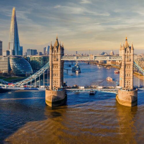 En bild av Londons stadssilhuett med Tower Bridge i förgrunden och moderna skyskrapor i bakgrunden, belyst av solnedgången.