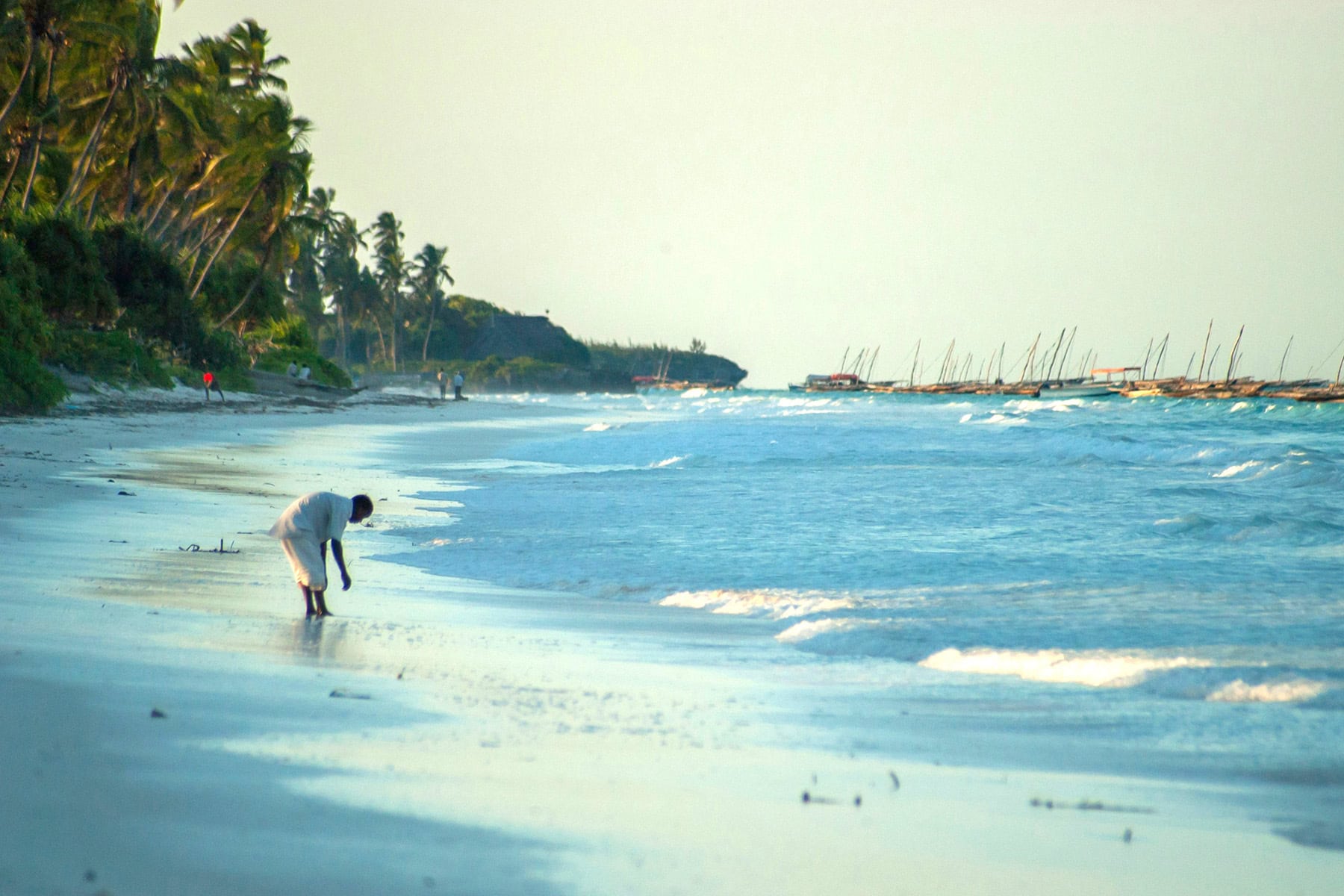 en vit strand med en zanzibar bor med båtar i bakgrunden