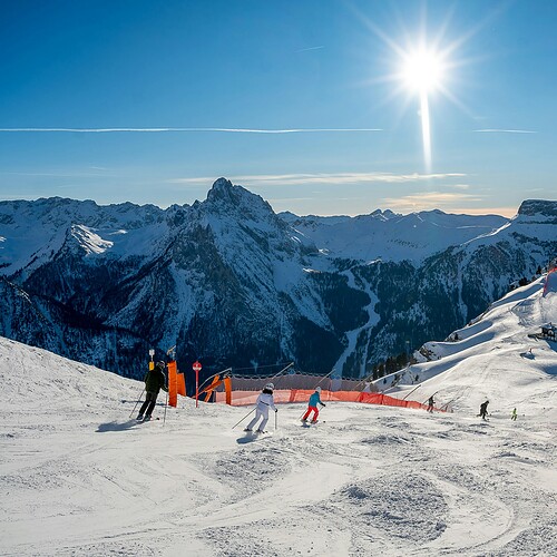 Skidåkare på snötäckta backar i Dolomiterna under klarblå himmel och sol.