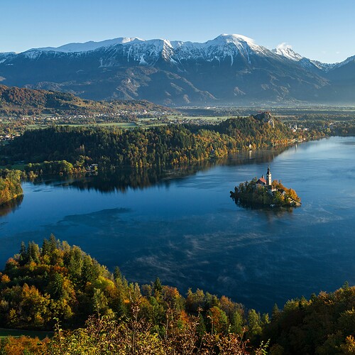 Färgstarkt sjölandskap i Slovenien med omgivande berg och höstfärger, perfekt för naturälskare och äventyrslystna resenärer.